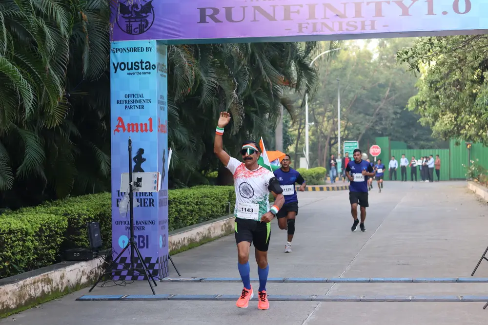 A finisher throwing both arms up at the Runfinity 1.0 arch